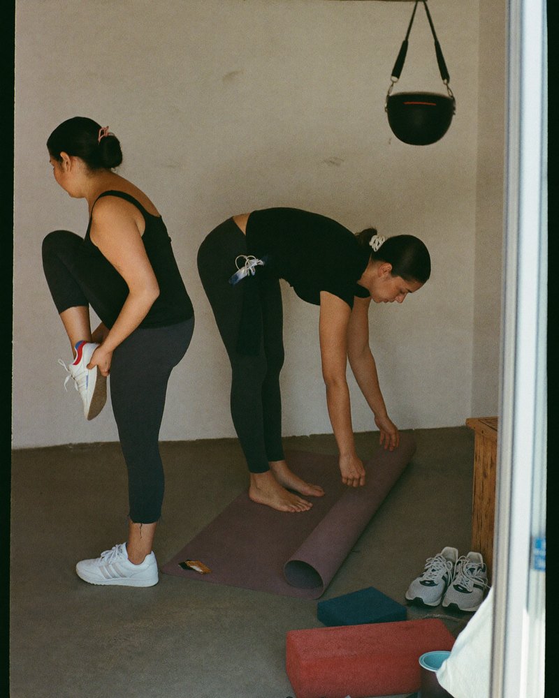 Maestra de yoga mexicana en sus treinta enrolla su tapete y platica con una alumna después de clase