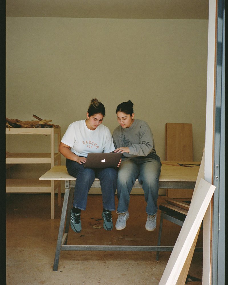 Dos hermanos mexicanos en su taller familiar de muebles comparten una laptop sobre la mesa de trabajo