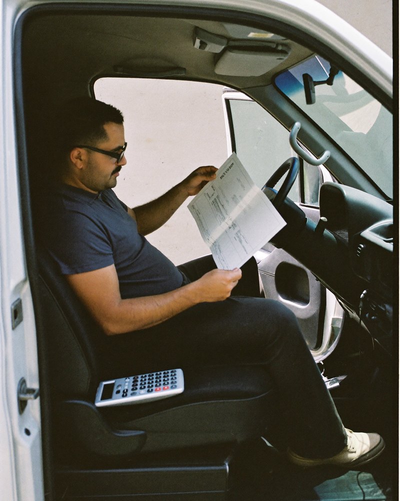 Plomero mexicano en sus cuarenta revisa una cotización en papel dentro de su camioneta de trabajo, con una calculadora en el asiento