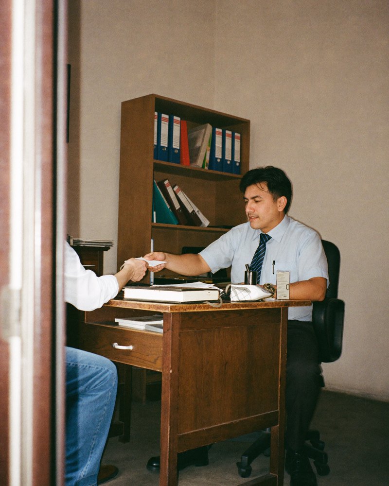 Abogado mexicano en sus treinta entrega su tarjeta de presentación a un cliente en su escritorio