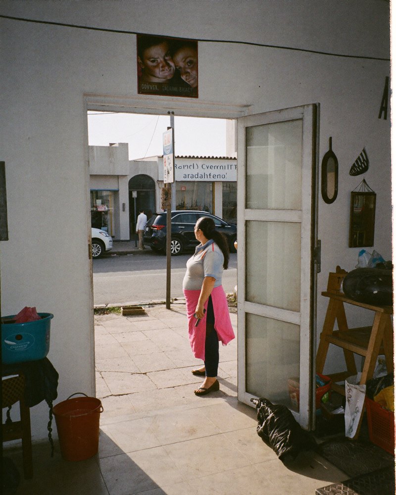 Óptica mexicana en sus 40 afuera de su local en una calle de barrio, celular en mano